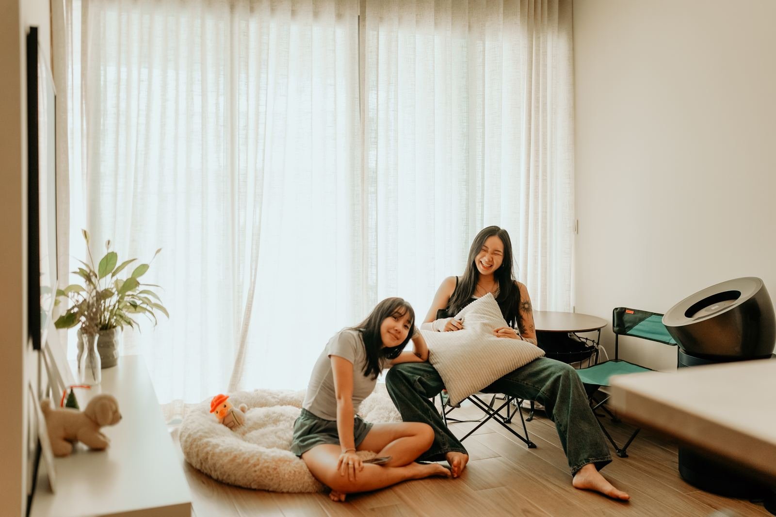 Two friends laughing by sheer curtains at home